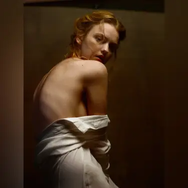 Woman with reddish-blonde hair in artistic portrait wearing draped white fabric against warm golden-brown backdrop, captured by 312 Elements Headshot Photography, portrait photographer in Chicago, IL