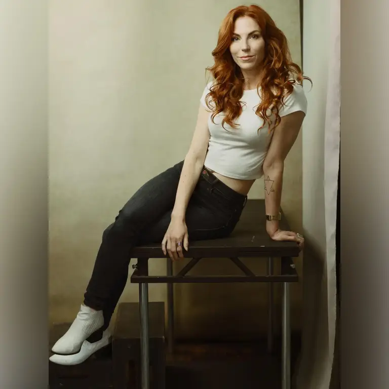 Professional portrait of Ashton Swinford with voluminous auburn curls seated on dark stool in neutral studio, photo by 312 Elements Headshot Photography, Chicago, IL portrait photographer
