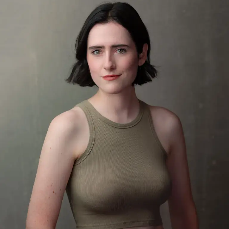 Improv performer headshot of a young woman in a sage green sleeveless top with direct eye contact against a grey background, photographed by Chicago headshot photographer Michael Schacht of 312 Elements