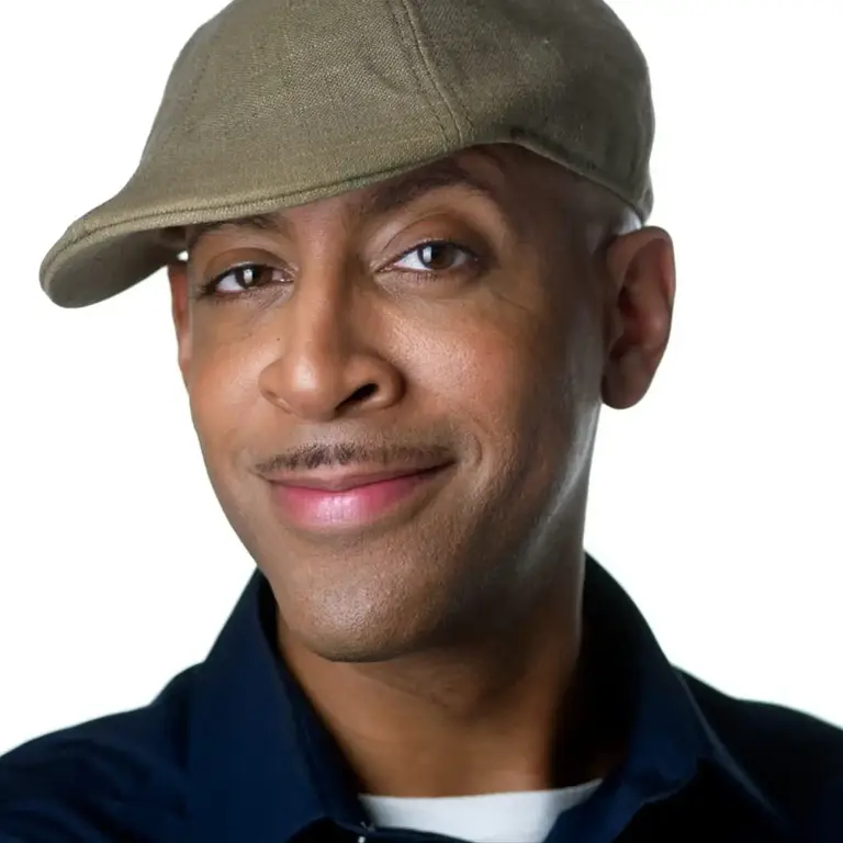 Comedian headshot of a man in an olive baseball cap and dark navy shirt with a friendly smile against a white background, photographed by Chicago headshot photographer Michael Schacht of 312 Elements