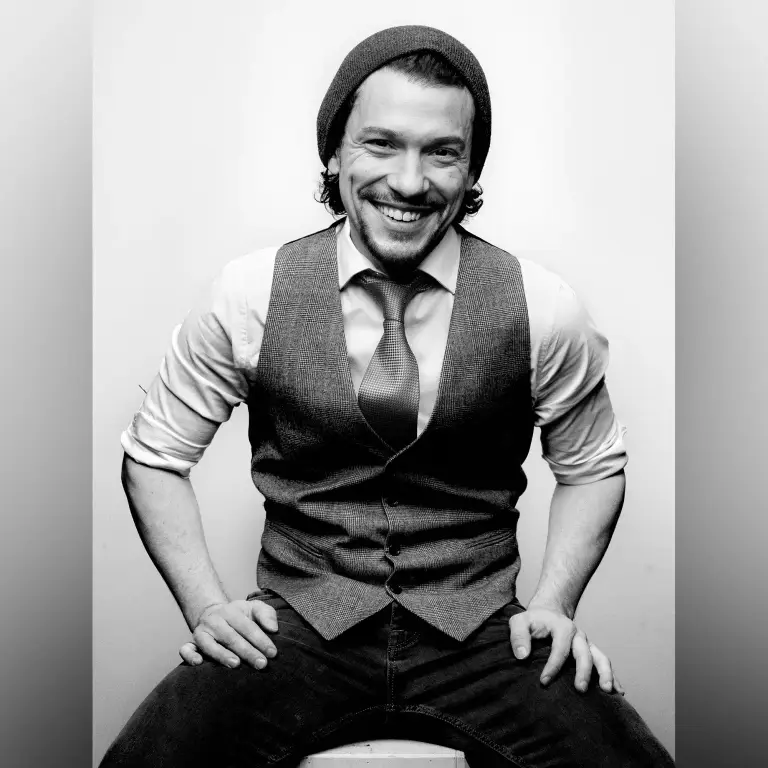 Black and white portrait of Miguel Cervantes with shoulder-length hair wearing gray vest and rolled-sleeve dress shirt in studio, portrait photographer 312 Elements Headshot Photography | Chicago, IL