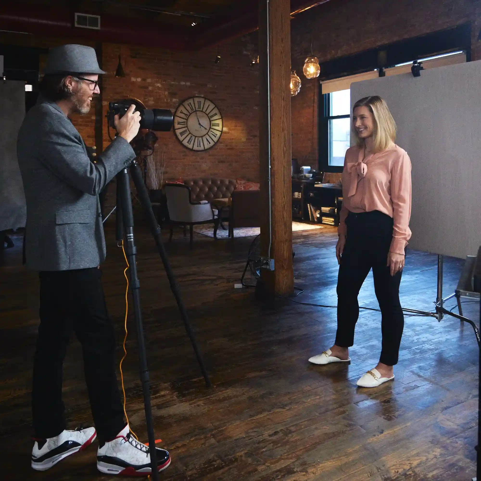 A stylish photographer in Air Jordans and a fedora captures a well-dressed client during a professional headshot branding photoshoot, showcasing a modern and trendy vibe.