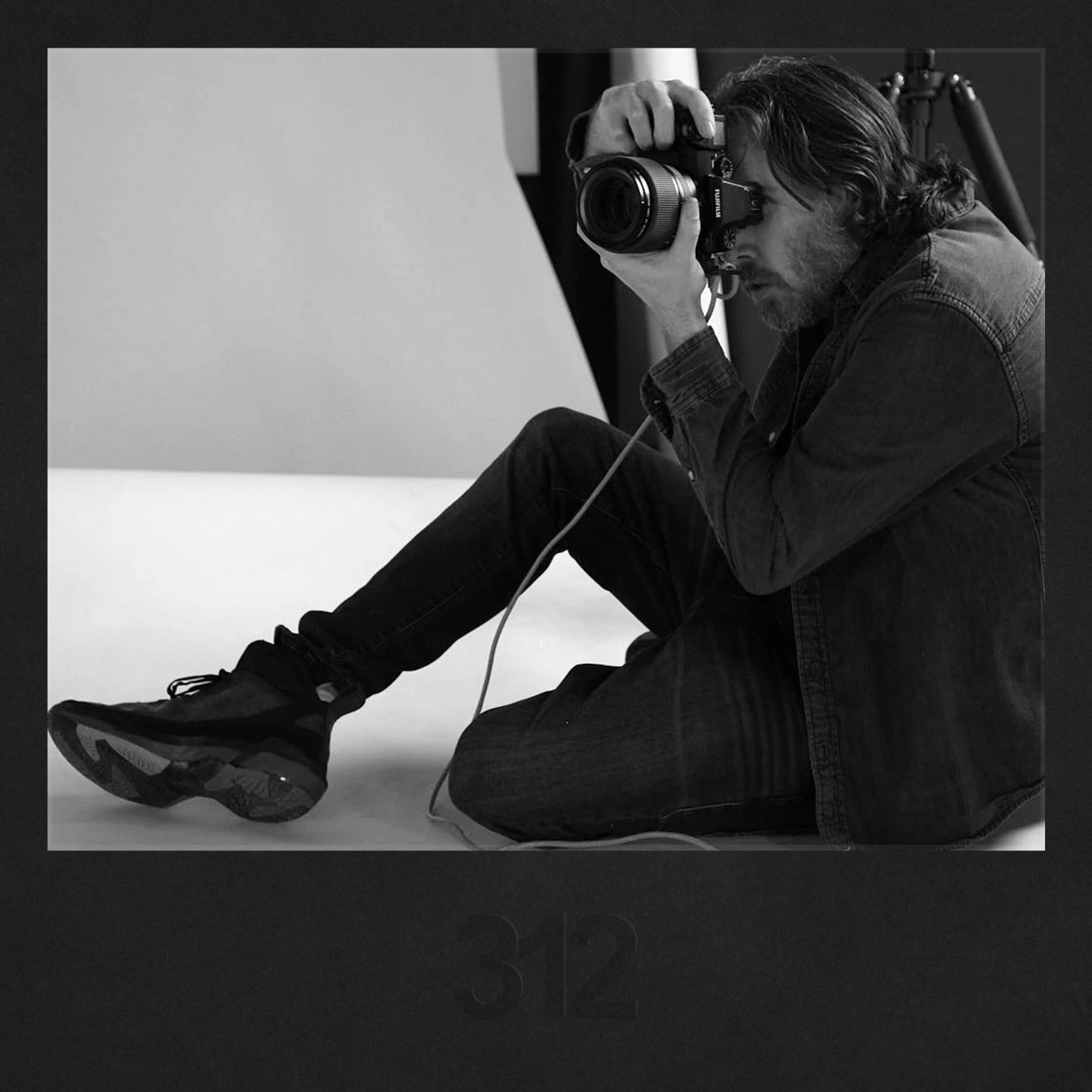 Headshot photographer sporting Air Jordans photographs a subject for a style matching assignment, set against a minimalist white background.