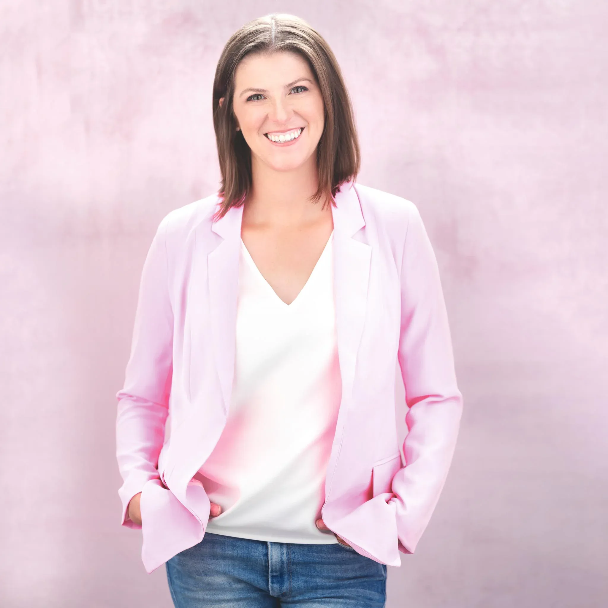 Professional headshot of a woman with a warm smile, wearing a stylish pink jacket against a light pink background.